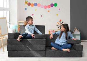 Smiling boy and girl sitting on a Mod Blox modular foam furniture couch in a playroom.