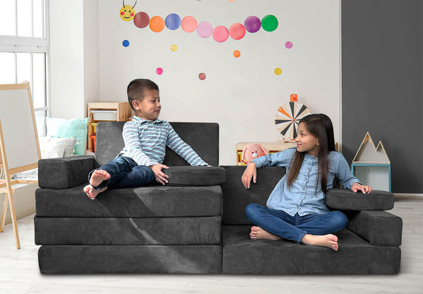 Smiling boy and girl sitting on a Mod Blox modular foam furniture couch in a playroom.